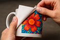 Hands peeling sublimation transfer paper to reveal a vivid design on a ceramic mug, crisp detail